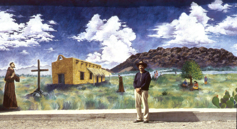 Mural depicting Spanish Mission.  Man stands in front of mural.