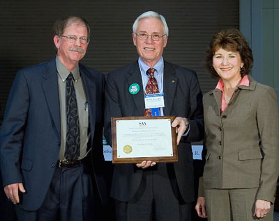A smiling man and a woman standing next to a man holding a plaque