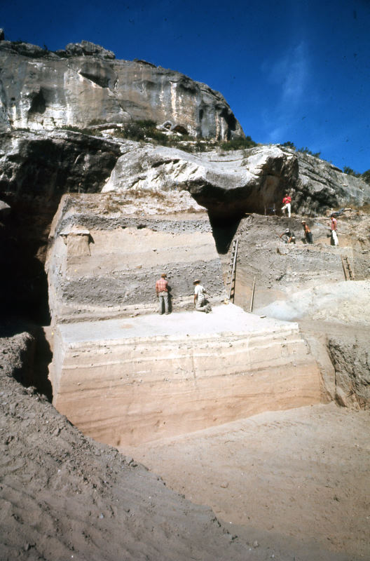 photograph of a cliff and high wall of stratified sediment with people excavating