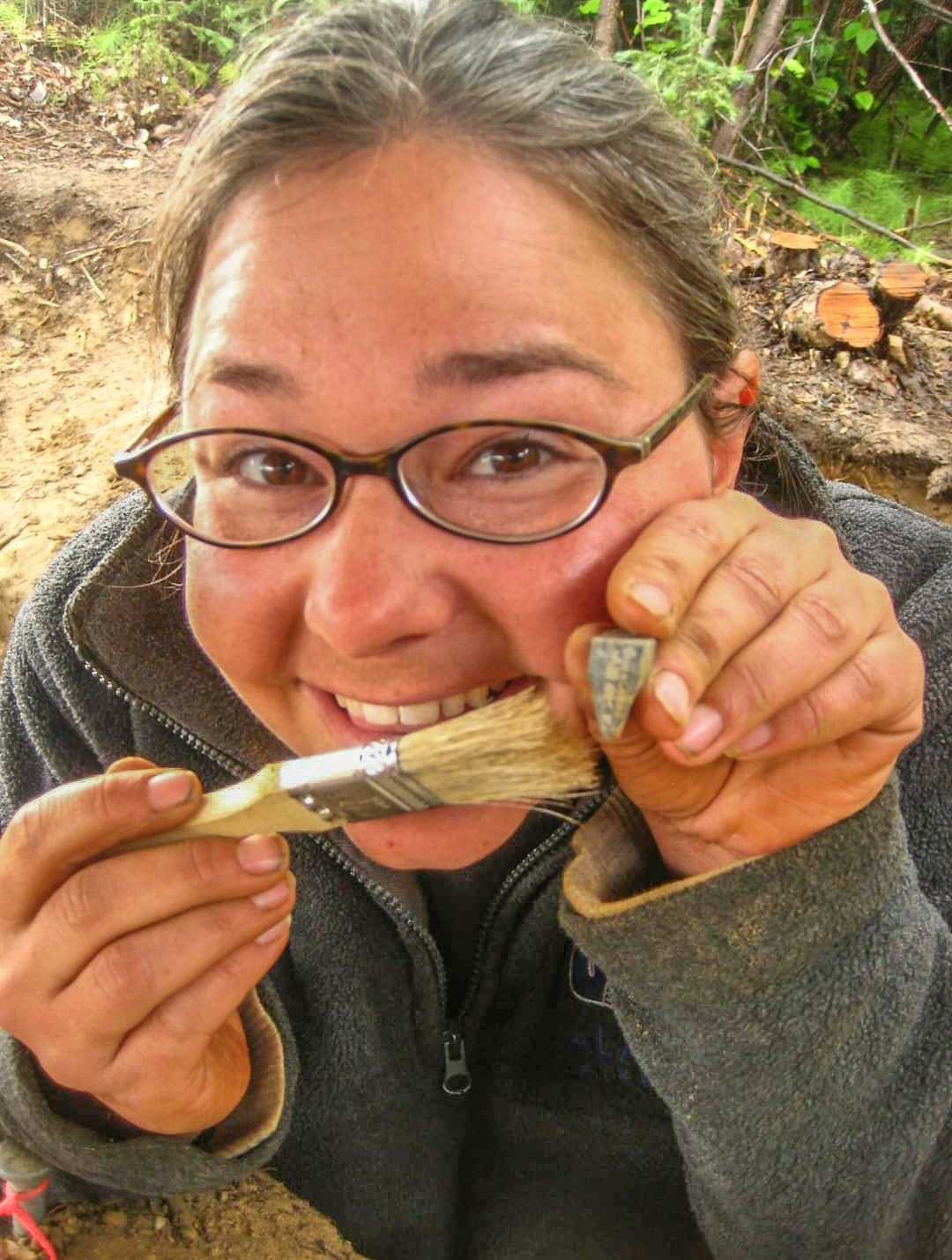 photograph of smiling woman holding an artifact and brush