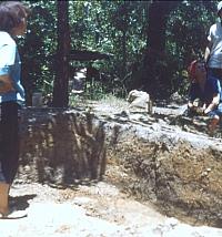 Dessamae Lorrain standing in excavation unit, Dee Ann Story in background facing camera. Visible in the profile is a thick layer of yellow-red clay that capped Feature 7, a trash midden.
