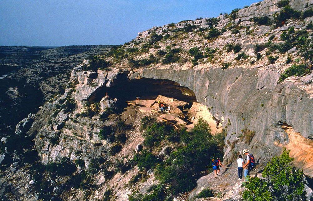 people walking across cliff towards rockshelter with impressive vista of canyonlands