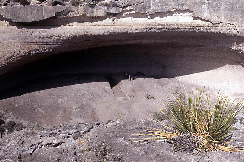 photo of large rockshelter with two archeologists near trench through center of deposits