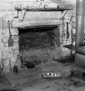 1935 photograph showing a wood stove, hearth, and fireplace mantle inside an old log cabin in Lauderdale County, Alabama