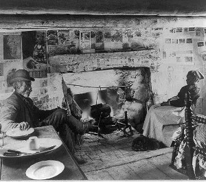 photograph from the Library of Congress collection taken around 1900 showing an older African American couple sitting by their fireplace in a log cabin