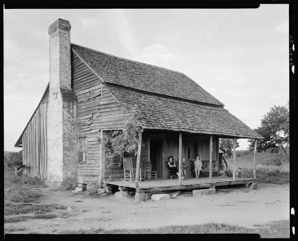 B&W photo of old house with porch and a brick chimney