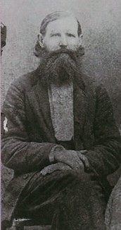 black and white photograph of a bearded man sitting with his legs crossed