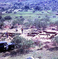 Photo showing scene across arid valley; in the midground is an archeological excavation with shirtless men workers.
