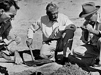 B&W photo of three men kneeling at dig site. 